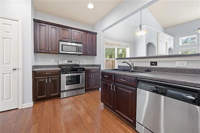 Kitchen with stainless steel appliances, dark brown cabinetry, pendant lighting, light wood finished floors, and recessed lighting