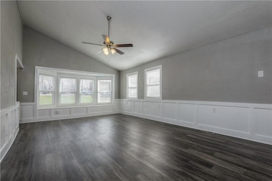 Unfurnished room with ceiling fan, vaulted ceiling, dark wood finished floors, a wainscoted wall, and a decorative wall