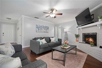 Living area with wood finished floors, ceiling fan, a fireplace, crown molding, and a textured ceiling