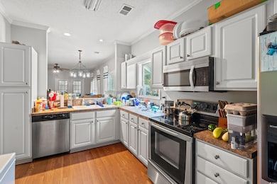 Kitchen with appliances with stainless steel finishes, crown molding, white cabinetry, light wood-type flooring, and recessed lighting