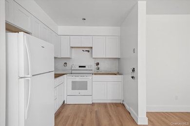 Kitchen with white appliances, white cabinetry, and light wood-style flooring