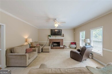 Carpeted living area featuring crown molding, plenty of natural light, ceiling fan, a brick fireplace, and baseboards