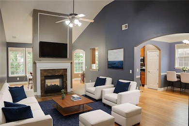 Living area with high vaulted ceiling, light wood finished floors, arched walkways, a high end fireplace, and ceiling fan
