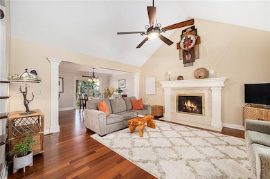 Living room with dark wood finished floors, high vaulted ceiling, decorative columns, a high end fireplace, and ceiling fan