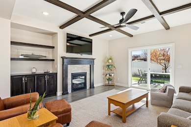 Living area featuring light wood-style flooring, a brick fireplace, coffered ceiling, beamed ceiling, and ceiling fan