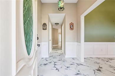 Hallway with wainscoting, marble finish floors, and a decorative wall