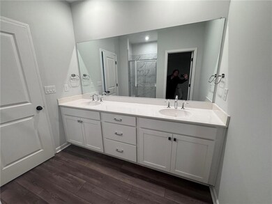 Bathroom featuring double vanity, a marble finish shower, and dark wood-style flooring