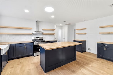 Kitchen with open shelves, backsplash, stainless steel gas range oven, light wood-type flooring, and extractor fan