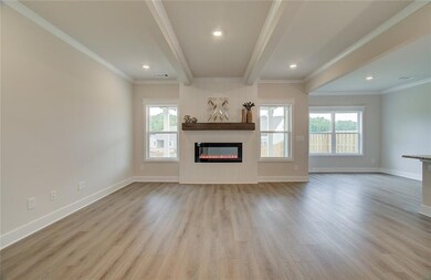 Unfurnished living room featuring wood finished floors, a glass covered fireplace, beam ceiling, baseboards, and ornamental molding