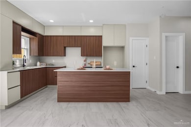 Kitchen featuring modern cabinets, a center island with sink, recessed lighting, light stone counters, and brown cabinets