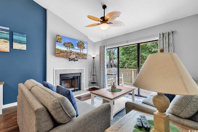 Living area featuring lofted ceiling, a textured ceiling, wood finished floors, a fireplace with raised hearth, and a ceiling fan