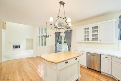 Kitchen featuring wooden counters, dishwasher, decorative light fixtures, light wood finished floors, and a glass covered fireplace