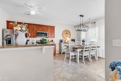 Kitchen featuring stainless steel appliances, stone counters, ceiling fan, light tile patterned floors, and brown cabinetry