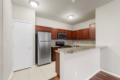 Kitchen featuring stainless steel appliances, a peninsula, light stone countertops, light tile patterned floors, and a breakfast bar