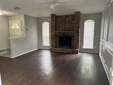 Unfurnished living room with a textured ceiling, ceiling fan, dark wood-style flooring, and a brick fireplace