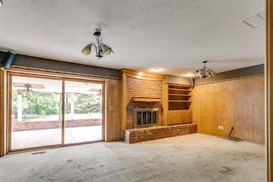 Unfurnished living room with a chandelier, a textured ceiling, carpet, a brick fireplace, and wood walls