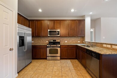 Kitchen with tasteful backsplash, appliances with stainless steel finishes, light tile patterned floors, light stone counters, and recessed lighting