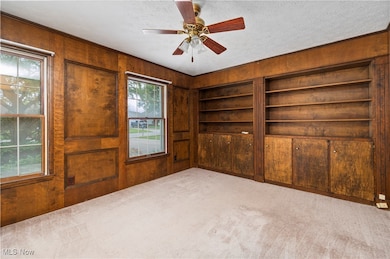 Spare room with wooden walls, built in shelves, carpet floors, a textured ceiling, and ceiling fan