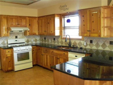 Kitchen featuring white appliances, brown cabinets, under cabinet range hood, and dark stone countertops