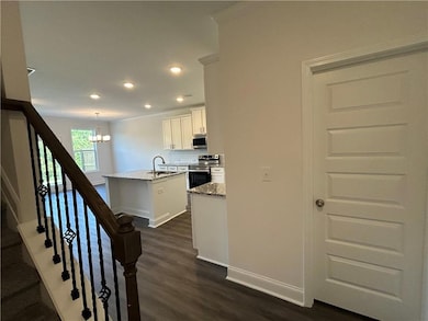 Kitchen with appliances with stainless steel finishes, a chandelier, dark wood-style flooring, white cabinetry, and light stone countertops
