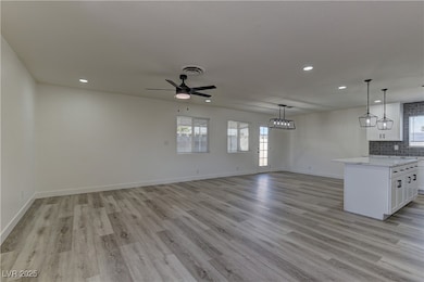 Kitchen with white cabinets, a ceiling fan, decorative backsplash, light wood-style floors, and open floor plan