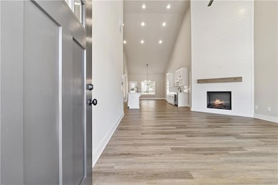 Unfurnished living room with high vaulted ceiling, light wood finished floors, a fireplace, baseboards, and recessed lighting