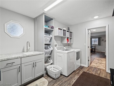 Expanded laundry/mud room area with counter space for folding clothes, utility sink, washer and dryer staying, and custom built-in shelving with laundry basket cubbies