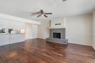 Unfurnished living room with a brick fireplace, wood finished floors, a textured ceiling, ceiling fan, and crown molding