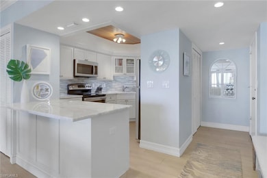 Kitchen featuring appliances with stainless steel finishes, a peninsula, white cabinets, glass insert cabinets, and recessed lighting