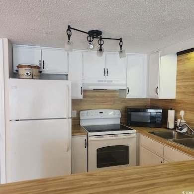 Kitchen featuring white appliances, white cabinetry, under cabinet range hood, a textured ceiling, and track lighting