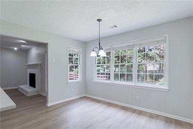 Unfurnished dining area featuring wood finished floors, a chandelier, a textured ceiling, and a brick fireplace