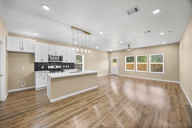 The open-concept living area and kitchen are thoughtfully designed with luxury vinyl plank flooring, recessed lighting, and a quartz-topped island that anchors the space. Oversized windows flood the room with natural light, creating a warm and inviting atmosphere.