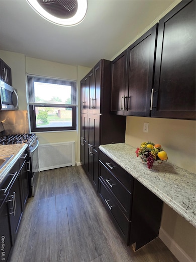 Kitchen featuring radiator, stove, dark wood finished floors, light stone countertops, and dark brown cabinetry