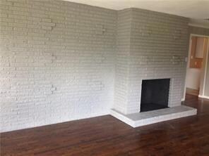 Unfurnished living room featuring brick wall, a brick fireplace, and dark wood-type flooring