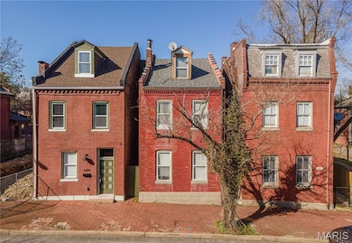 View of front facade with brick siding, a shingled roof, and fence
