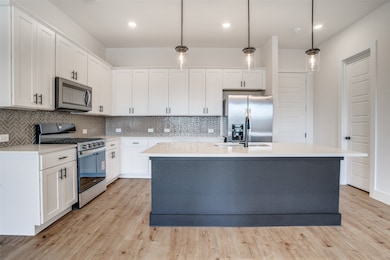 Kitchen with appliances with stainless steel finishes, decorative light fixtures, light wood-type flooring, backsplash, and white cabinets