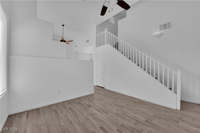 Unfurnished living room with a ceiling fan, light wood finished floors, high vaulted ceiling, and stairs