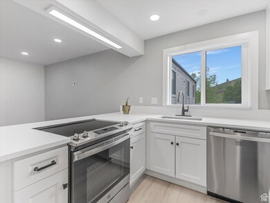 Kitchen featuring stainless steel appliances, white cabinets, recessed lighting, light wood-type flooring, and light stone countertops