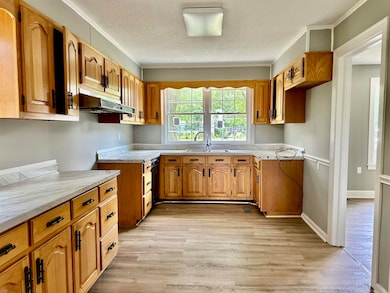 Kitchen with under cabinet range hood, light wood finished floors, light countertops, a sink, and a textured ceiling
