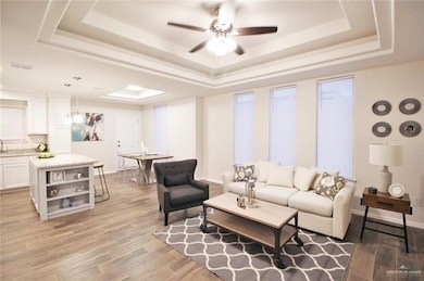 Living area with light wood finished floors, a tray ceiling, and ceiling fan
