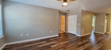 Empty room with dark wood-type flooring, a ceiling fan, baseboards, and a textured ceiling
