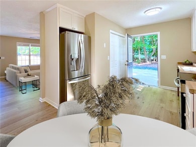 Kitchen with stainless steel refrigerator with ice dispenser, white cabinets, light wood-type flooring, a textured ceiling, and stove