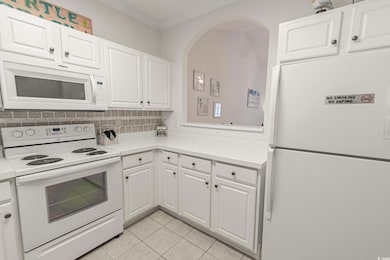 Kitchen featuring white appliances, crown molding, tasteful backsplash, light countertops, and white cabinetry