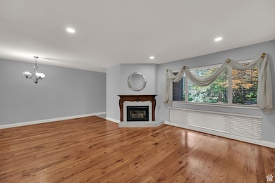 Unfurnished living room with wood finished floors, a fireplace with raised hearth, recessed lighting, and a chandelier
