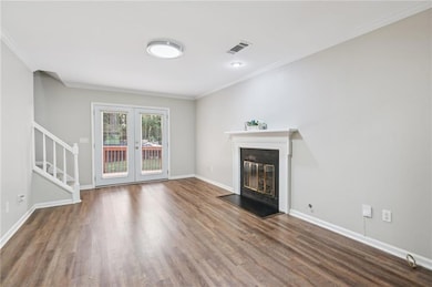 Unfurnished living room featuring stairs, wood finished floors, french doors, a glass covered fireplace, and ornamental molding