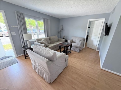 Living room with light wood-type flooring, a textured ceiling, and baseboards