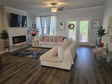 Living room featuring wood finished floors, ornamental molding, a glass covered fireplace, a ceiling fan, and baseboards