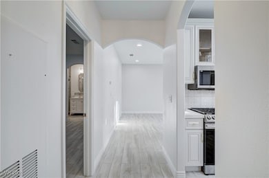 Hall with arched walkways, light wood finished floors, and recessed lighting