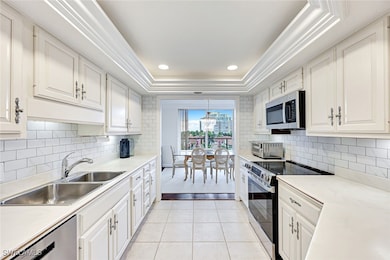 Kitchen with a tray ceiling, stainless steel appliances, light countertops, light tile patterned flooring, and recessed lighting