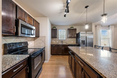 Kitchen with appliances with stainless steel finishes, dark brown cabinets, decorative light fixtures, and light wood-style flooring